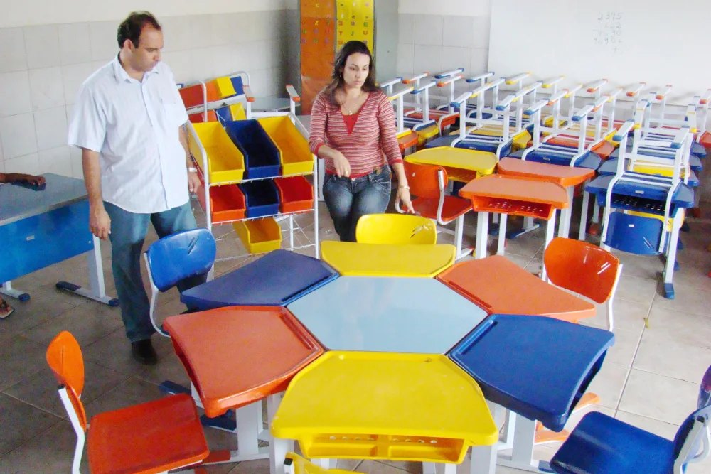 Ari Saraiva em sala de aula recém-equipada, entre carteiras e mesas coloridas novas.