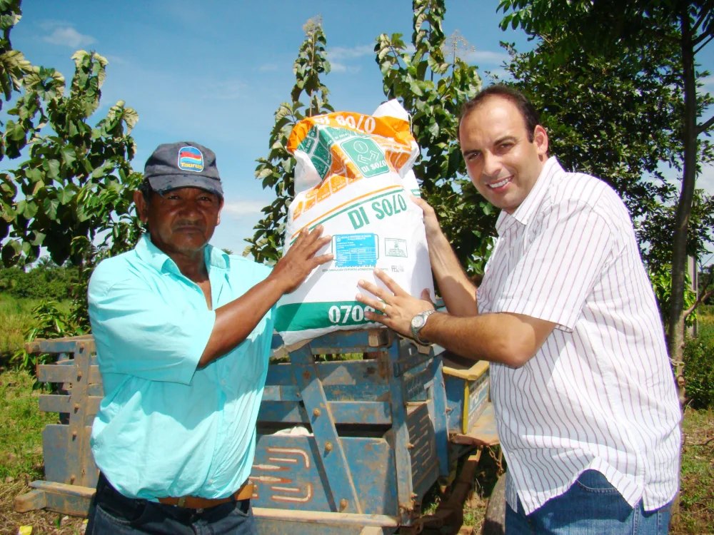 Ari Saraiva entregando um saco de sementes a um produtor rural sobre a carroceria de um trator.